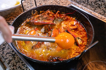 Induction cooking of a lobster rice paella. Metal and plastic ladle stirs the contents of the paella prepared at home with care and love. 