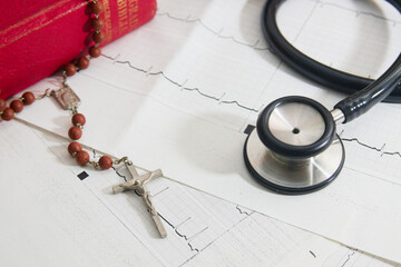 Flat lay of a cardiogram on which there is a crucifix, a stethoscope and a bible