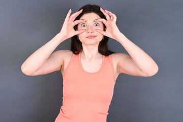 Caucasian woman wearing orange T-shirt over grey wall keeping eyes opened to find a success opportunity.