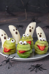 Spooky banana ghosts monsters and green kiwi monsters for Halloween party on brown background decorated with spiders and bats