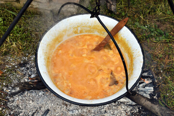 Outdoor cooking a meal. Cooking outdoors in cast-iron cauldron. Cooking meat on a fire. Food in a...