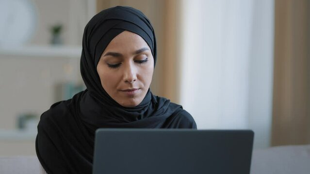 Focused ethnic female muslim arabian young woman girl islamic student businesswoman freelancer sits at home work on computer online chat search information data analyze develop web design e-commerce