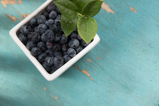 White container of blueberries on a light blue, chippy paint background.