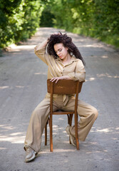portrait of a beautiful brunette curly hair woman sitting on the chair in park