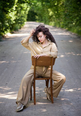 portrait of a beautiful brunette curly hair woman sitting on the chair in park