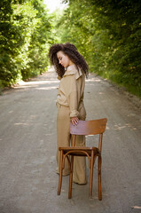 Fototapeta na wymiar portrait of a beautiful brunette curly hair woman staying near the chair in park