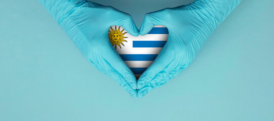 Doctors hands wearing blue surgical gloves making hear shape symbol with Uruguay flag