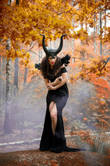 Naklejka premium Concept of Halloween and fantasy horror. Cosplay on Maleficent demonic - starring. Face of beautiful woman from a fairytale in autumn forest. Beautiful girl dressed up as devil