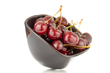 Several sweet cherries in a black ceramic plate, close-up, isolated on a white background.