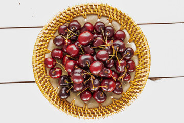 Several sweet cherries on a ceramic plate on a wooden table, close-up, top view.