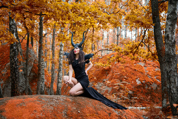 Naklejka premium Concept of Halloween and fantasy horror. Cosplay on Maleficent demonic - starring. Face of beautiful woman from a fairytale in autumn forest. Beautiful girl dressed up as devil