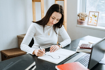 Female Accountant writing to question mark in a notepad on the background of laptop and calculator