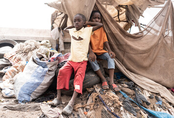 Two young desperate African children sitting on tires and waste on a huge garbage dump in a village...
