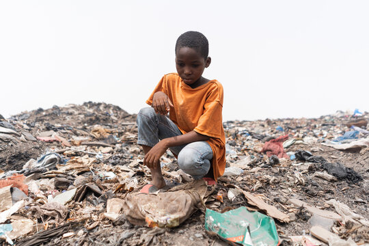 Despairing African child sitting on a garbage dump, looking at the plastic waste. Environmental justice concept.