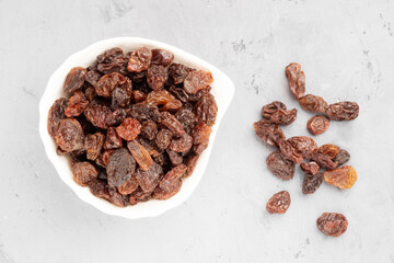Raisin in white ceramic bowl and bunch on gray concrete background. Macro. Vegetarian concept