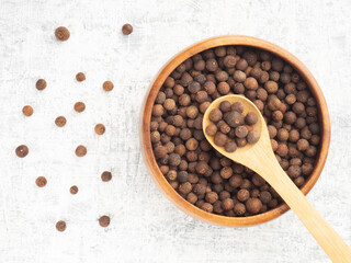 Spice Allspice (Jamaica pepper, Pimento) in wooden bowl, spoon, bunch on white concrete background. Macro. Flat lay. Healthy eating concept