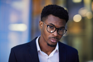 Portrait of serious confident young smart Afro-American entrepreneur with beard wearing eyeglasses and suit