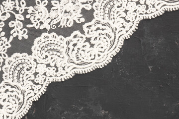 White lace on black concrete background diagonally with copy space. Contrast of tender and rough