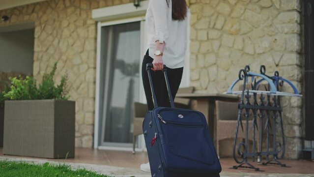 Woman traveler pulling rolling baggage, arriving to holiday resort hotel or motel, moving, traveling.