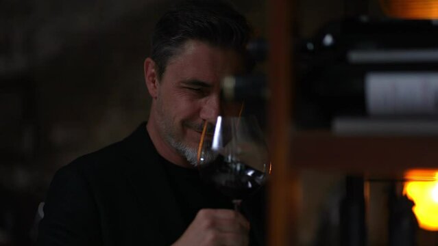 Middle aged man tasting, drinking wine. Wine expert rating a glass of red wine. Professional sommelier satisfied.
