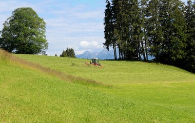Bauer mit landwirtschaftlichem Gerät mäht die Wiese und macht Heu. Hügeliges Alpenvorland,...