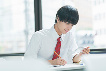 教室でスマートフォンを見る男性高校生