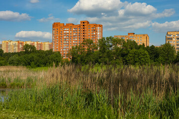 Fototapeta na wymiar Big house and summer city park with trees in the sunny daytime, blue sky. A park next to a residential area