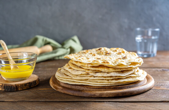 Homemade Indian flat breads Chapati or Roti on wooden background with butter ghee, water, rolling pin and napkin