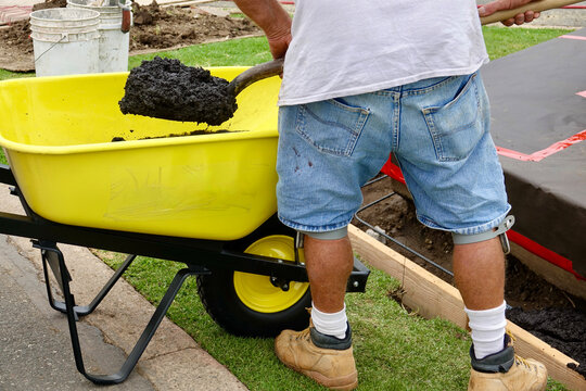 Construction Worker Using A Shovel To Move Concrete From Wheel Barrow