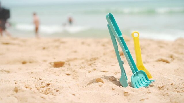 Set of plastic beach toys on sand near sea. Space for text. Plastic toys for children yo play on beach. Blurred ocean beach background with people