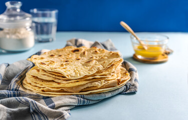 Homemade Indian flat breads Chapati or Roti on kitchen towel over blue background with butter ghee, water, flour.