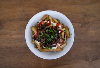 Top view of fried potatoes with cream cheese, crispy bacon, green onion and sweet chili in a white bowl on the wooden table. 