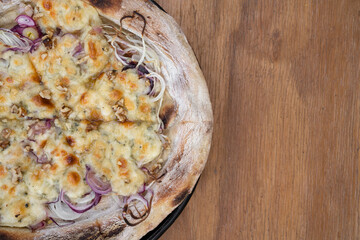 Top view of a homemade pizza with cheese and red onion, in a pizza pan on the wooden table. 