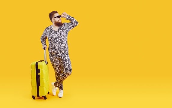 Fat Traveler In Funny Costume Posing On Copy Space Background. Chubby Plus Size Bearded Man Wearing Leopard PJs And Cool Sunglasses Standing With Holiday Suitcase On Yellow Copyspace Studio Backdrop