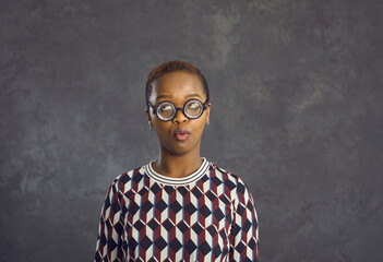 Funny millennial gen z African American girl in round glasses on black studio background look at copy space. Young ethnic woman in spectacles have eyesight problem. Optician, eyewear concept. - Powered by Adobe