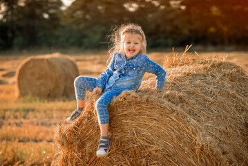 Naklejka na ściany i meble girl is sitting on a haystack and smiling 