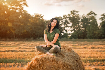 Naklejka na ściany i meble woman is sitting on a haystack at the sunset