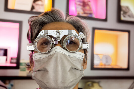 Mature Asian man wearing phoropter as eye test device for vision correction at eyeglasses store