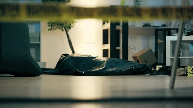 Body of dead person lying on floor covered with plastic corpse bag, murder scene