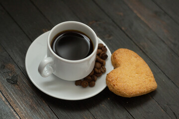 a cup of coffee with coffee beans and love cookie on wooden surface.Valentine day holiday