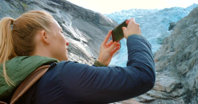 4k video footage of a young woman standing and using her cellphone to photography Briksdal Glacier