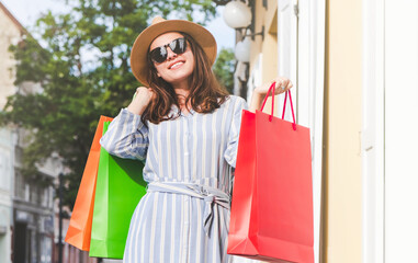 Woman in hat standing on the street and holding purchases in hand.