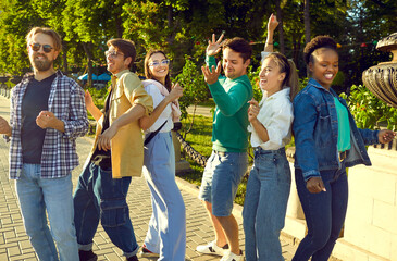Group of happy young people meet up at the city park on Sunday. Diverse bunch of cheerful, funny, excited friends in casual summer clothes dancing, having fun and enjoying their day off together