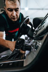 Professional worker cleaning car interior and dashboard, car detailing (or valeting) concept. Selective focus. Ultra wide angle shot.