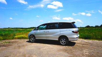 Fototapeta na wymiar Silver modern minivan. Japanese car. Located in nature. Sunny day. Blue sky. Travel by car. Family transport. Side view.