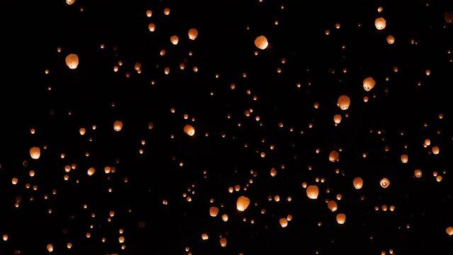 View of sky lanterns floating up through the sky at night during celebration event.