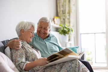 Elderly couple looking at a photo album while sitting on a sofa
