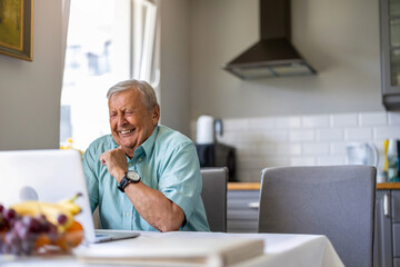 Elderly man using laptop at kitchen table
