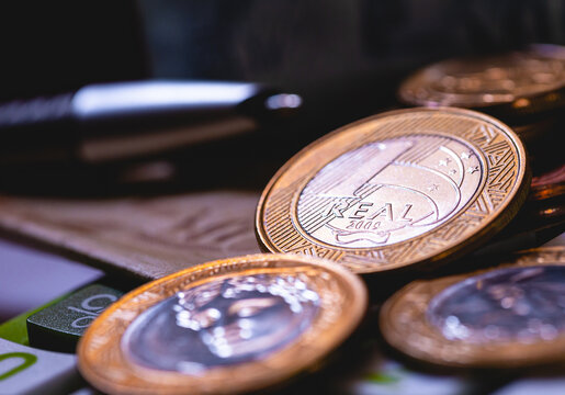 Moedas e c&eacute;dulas do Real Brasileiro sobre uma calculadora e uma caneta quebrada na composi&ccedil;&atilde;o da imagem. Representa&ccedil;&atilde;o da crise econ&ocirc;mica. Conceitos de economia brasileira, infla&ccedil;&atilde;o e impostos.