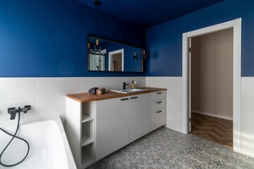 Fototapeta na wymiar Modern bathroom with blue walls, white furniture and a bathtub